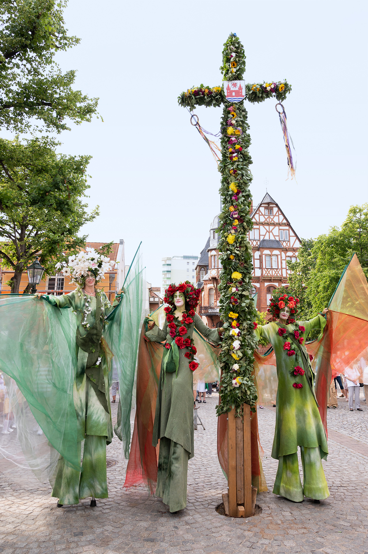 Foto: 3 Stelzenläuferinnen in blumigen Kostümen an der Mittsommerstange