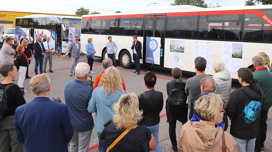 Foto: zahlreiche Personen stehen im Halbkreis um den Referenten vor einem Bus