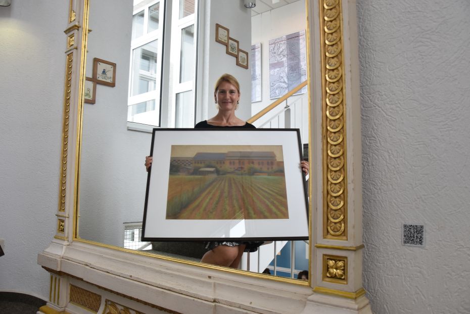 Frau steht mit Bild, auf dem Tabakscheunen zu sehen sind, vor dem Spiegel.