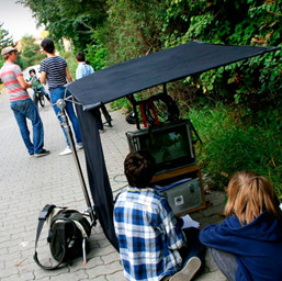 Foto: Zwei sitzende Jungen beobachten Dreharbeiten über einen Monitor.