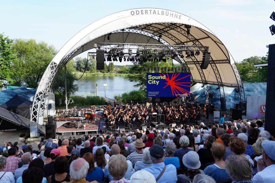 Viele Menschen sitzen vor einer Wasserbühne und hören Musik.