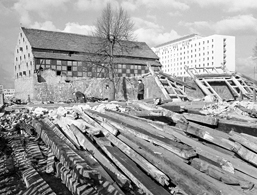 Foto: Balken einer abgerissenen Tabakscheune, dahinter ein Neubau