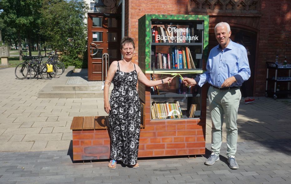 Foto: 2 Personen fassen die Schleife am Bücherschrank an.