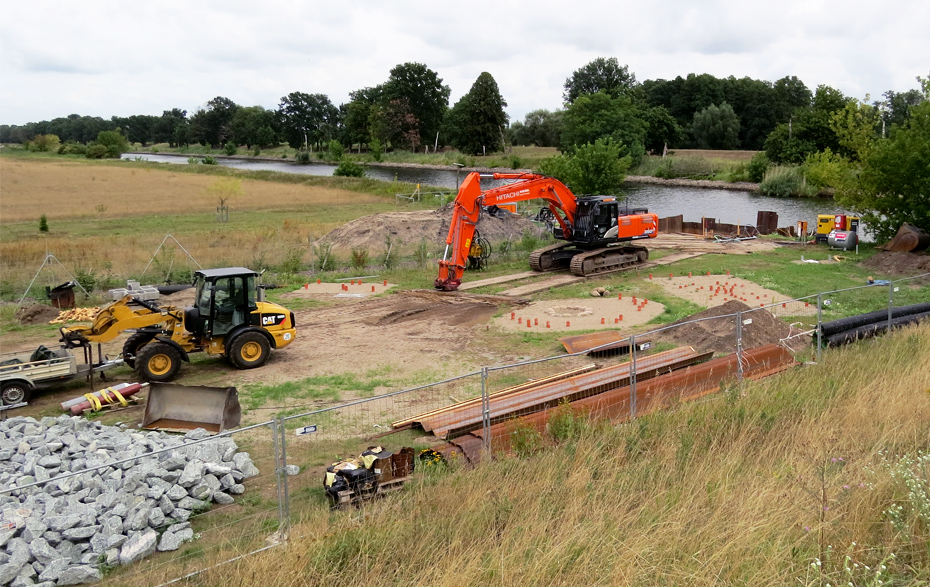 Foto: Baufahrzeuge, Baumaterial und Fundamente im eingezäunten Bereich am Kanal