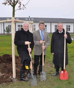 Foto: Drei Männer stehen vor einem frisch gepflanzten Baum mit Spaten.