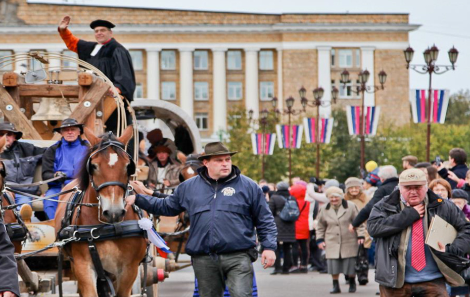 Planwagen fahren durch eine Stadt und werden von Menschen bejubelt