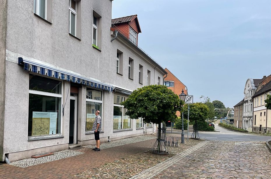 Foto: Straßenansicht mit Geschäften. In den Geschäften stehen Ausstellungstafeln mit historischen Karten.