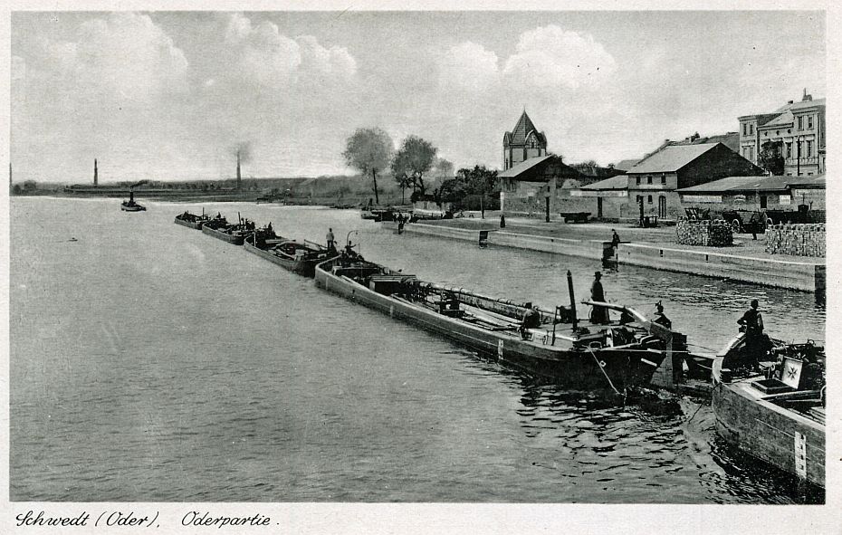 Lastschiffe fahren an einer Kaimauer mit dahinter liegender Stadt vorbei.