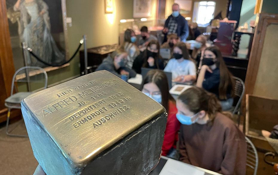 Stein mit Messingplatte, im Hintergrund lesen und recherieren Menschen