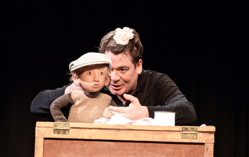 Foto: Schauspieler und Puppe hinter einer Kiste Foto: Schauspieler und Puppe hinter einer Kiste