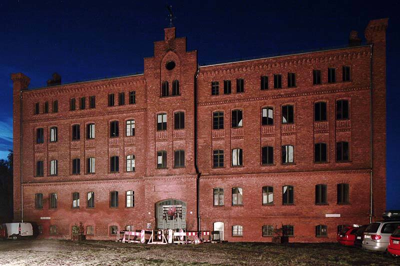 Foto: Tabakfabrik nachts mit beleuchtetem, abgesperrtem Eingang