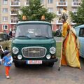 Foto: Stelzenfrau steht neben einem grünen Barkas, auf der anderen Seite ein kleiner Junge