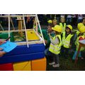 Foto: Kinder mit Bauhelmen und gelben Westen befestigen gemeinsam mit dem Erzieher Zettel an dem Mini-Dachstuhl.