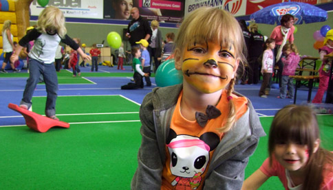 Foto: geschminktes Mädchen, im Hintergrund spielende Kinder