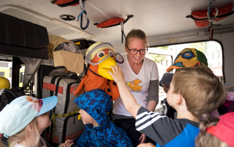 Foto: Frau mit Spatzenpuppe, umringt von Kindern in einer Feuerwehr Foto: Frau mit Spatzenpuppe, umringt von Kindern in einer Feuerwehr