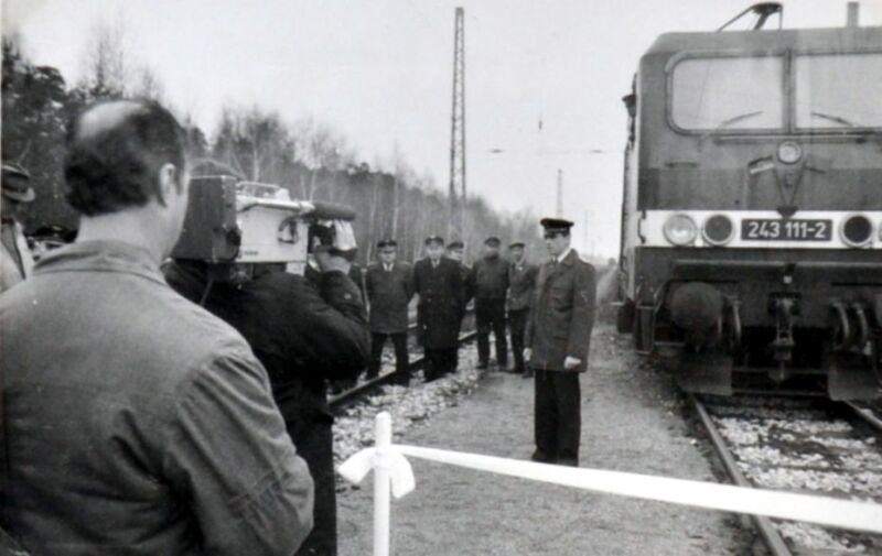 Menschen auf einem Bahnsteig, daneben ein Gleis mit E-Lok