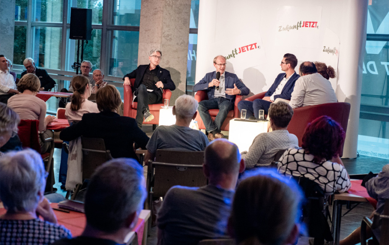 Foto: 5 Personen im Podium und Publikum drumherum Foto: 5 Personen im Podium und Publikum drumherum