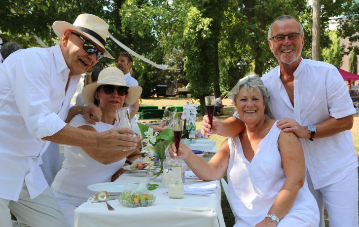 Foto: 4 weiß gekleidete Personen an einer weiß gedeckten Tafel im Park