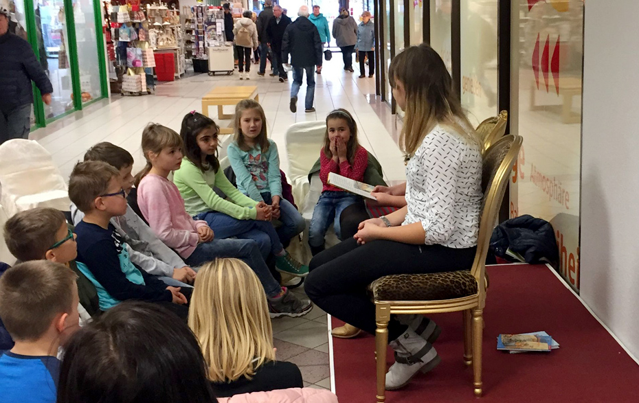 Foto: Kindergruppe sitzt vor einer Vorleserin in den Passagen